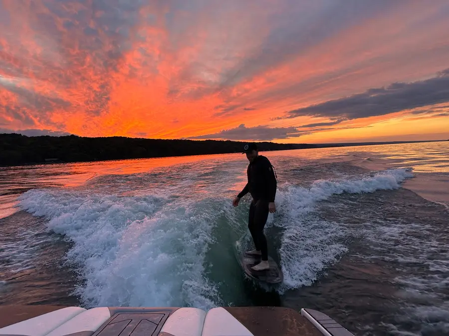 A wakesurfer riding beneath a vivid red and orange sunset