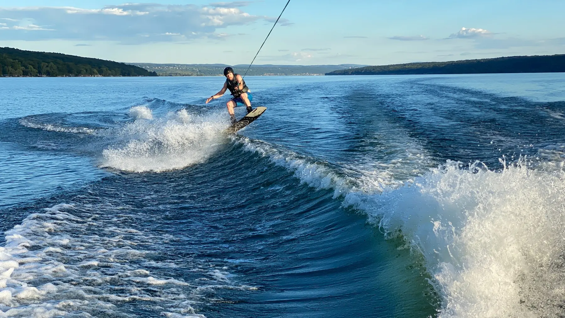 A helmeted wakeboarder riding across a clean evening wake